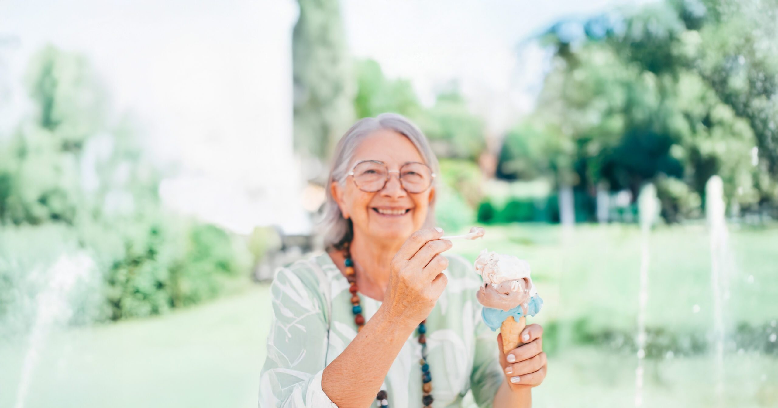 senior woman sitting outside in the summer next to a fountain enjoying an ice cream cone